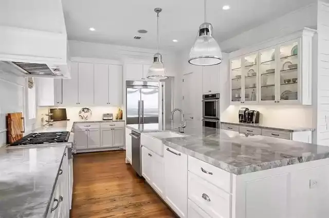 Kitchen remodel in Galveston with marble countertops, white cabinets and pendant lights