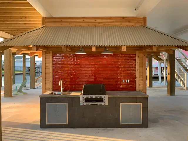 Covered outdoor kitchen with grill, sink and red tile backsplash under a Galveston stilt home